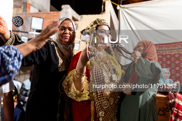 A bedouin bride dressed in traditional bedouin dress and head cover sits on a raised chair as she celebrates her wedding together with her f...