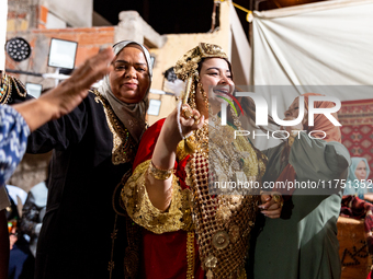 A bedouin bride dressed in traditional bedouin dress and head cover sits on a raised chair as she celebrates her wedding together with her f...