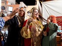 A bedouin bride dressed in traditional bedouin dress and head cover sits on a raised chair as she celebrates her wedding together with her f...