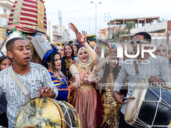 Bedouin wedding guests  dressed in traditional bedouin dresses and head covers dance and sing on the street as they escort the bride to her...