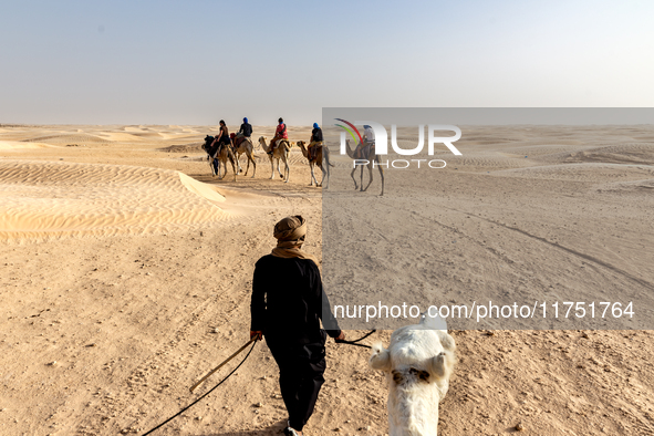 Tourists ride on camels in a caravan on dunes of Eastern Sahara desert on a sunny day on October 30, 2024 near Douz, Tunisia. 