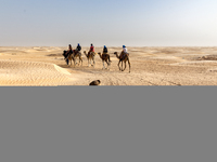 Tourists ride on camels in a caravan on dunes of Eastern Sahara desert on a sunny day on October 30, 2024 near Douz, Tunisia. (