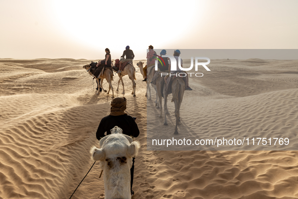 Tourists ride on camels in a caravan on dunes of Eastern Sahara desert on a sunny day on October 30, 2024 near Douz, Tunisia. 