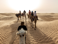 Tourists ride on camels in a caravan on dunes of Eastern Sahara desert on a sunny day on October 30, 2024 near Douz, Tunisia. (