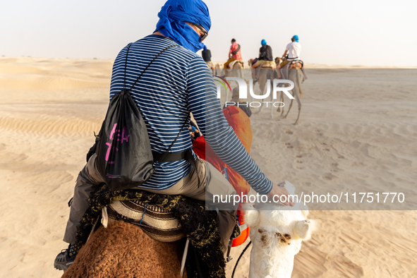 Tourists ride on camels in a caravan on dunes of Eastern Sahara desert on a sunny day on October 30, 2024 near Douz, Tunisia. 