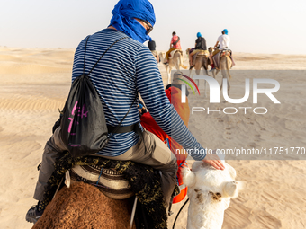 Tourists ride on camels in a caravan on dunes of Eastern Sahara desert on a sunny day on October 30, 2024 near Douz, Tunisia. (