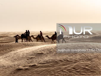 Tourists ride on camels in a caravan on dunes of Eastern Sahara desert on a sunny day on October 30, 2024 near Douz, Tunisia. (