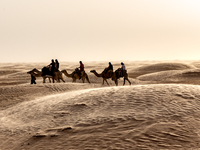 Tourists ride on camels in a caravan on dunes of Eastern Sahara desert on a sunny day on October 30, 2024 near Douz, Tunisia. (