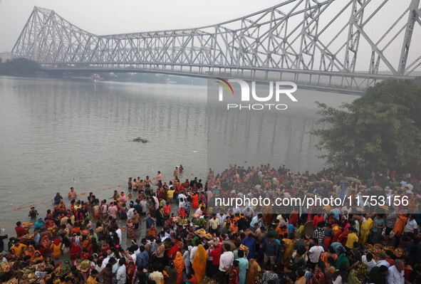 Hindu devotees hold offerings as they stand in the water of the river Ganges during the early morning in front of the iconic Howrah Bridge t...