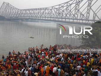 Hindu devotees hold offerings as they stand in the water of the river Ganges during the early morning in front of the iconic Howrah Bridge t...