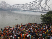 Hindu devotees hold offerings as they stand in the water of the river Ganges during the early morning in front of the iconic Howrah Bridge t...