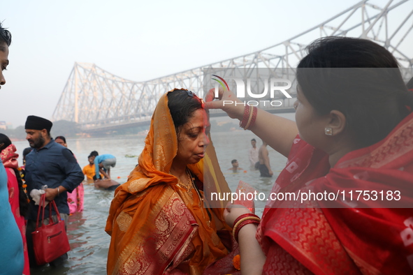 A Hindu woman has her forehead smeared with vermilion powder in front of the Howrah Bridge as she worships the Sun god in the waters of the...