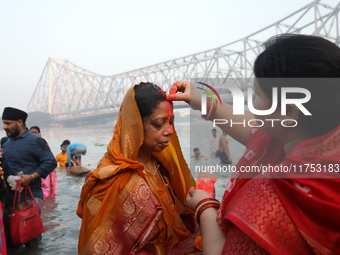 A Hindu woman has her forehead smeared with vermilion powder in front of the Howrah Bridge as she worships the Sun god in the waters of the...