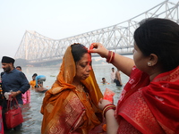 A Hindu woman has her forehead smeared with vermilion powder in front of the Howrah Bridge as she worships the Sun god in the waters of the...