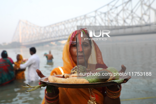 A Hindu devotee holds offerings as she stands in the water of the river Ganges during the early morning in front of the iconic Howrah Bridge...