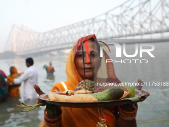 A Hindu devotee holds offerings as she stands in the water of the river Ganges during the early morning in front of the iconic Howrah Bridge...