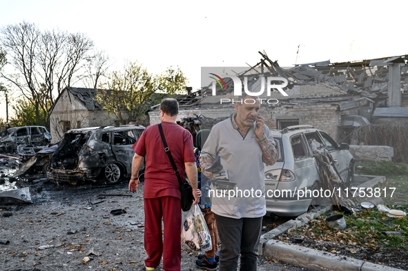 People stand by burnt-out cars outside an oncology dispensary damaged by a Russian guided bomb attack in Zaporizhzhia, Ukraine, on November...