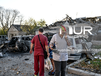 People stand by burnt-out cars outside an oncology dispensary damaged by a Russian guided bomb attack in Zaporizhzhia, Ukraine, on November...