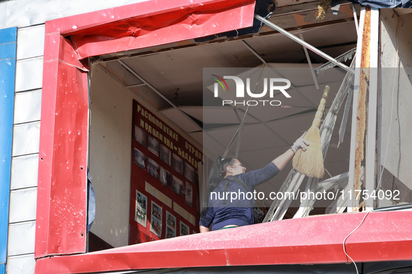 A woman removes debris from a building housing both a school and kindergarten, which is damaged by a shock wave during an overnight Russian...