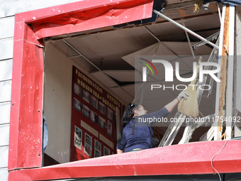 A woman removes debris from a building housing both a school and kindergarten, which is damaged by a shock wave during an overnight Russian...