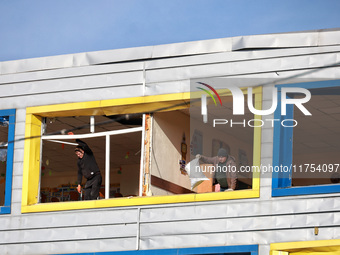 People remove debris from a building housing both a school and kindergarten, which is damaged by a shock wave during an overnight Russian dr...