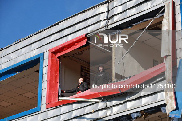 Two men remove debris from a building housing both a school and kindergarten, which is damaged by a shock wave during an overnight Russian d...