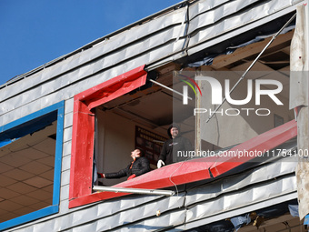 Two men remove debris from a building housing both a school and kindergarten, which is damaged by a shock wave during an overnight Russian d...