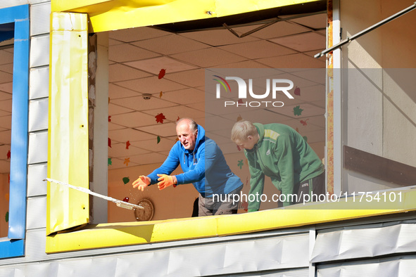 Two men remove debris from a building housing both a school and kindergarten, which is damaged by a shock wave during an overnight Russian d...