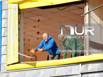 Two men remove debris from a building housing both a school and kindergarten, which is damaged by a shock wave during an overnight Russian d...