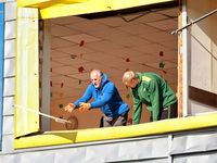 Two men remove debris from a building housing both a school and kindergarten, which is damaged by a shock wave during an overnight Russian d...