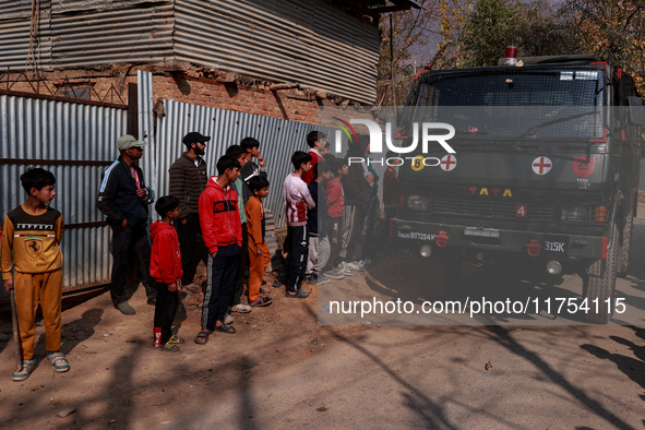 Children, young men, and elderly men watch as Indian army vehicles leave the encounter site after killing two militants in Sopore, Jammu and...