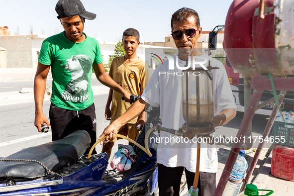 Young men tank their motorcycle from a mobile tank in Tozeur in central Tunisia on October 28, 2024. 