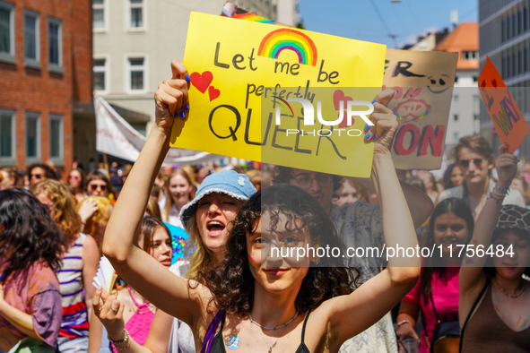 A young woman holds up a bright yellow sign that reads ''Let me be perfectly QUEER'' with a rainbow and hearts during the Christopher Street...