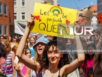 A young woman holds up a bright yellow sign that reads ''Let me be perfectly QUEER'' with a rainbow and hearts during the Christopher Street...