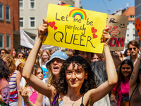 A young woman holds up a bright yellow sign that reads ''Let me be perfectly QUEER'' with a rainbow and hearts during the Christopher Street...