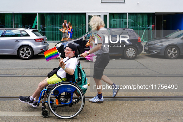 A participant in a wheelchair waves a rainbow flag with a smile while being pushed by a man during the Christopher Street Day Parade in Muni...