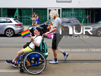 A participant in a wheelchair waves a rainbow flag with a smile while being pushed by a man during the Christopher Street Day Parade in Muni...