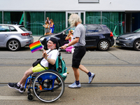 A participant in a wheelchair waves a rainbow flag with a smile while being pushed by a man during the Christopher Street Day Parade in Muni...