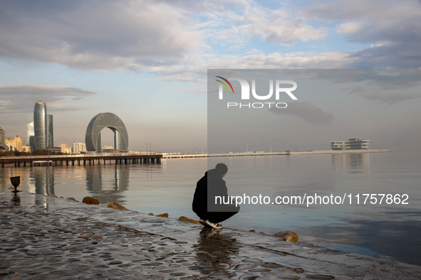 A man sits on Caspian Sea Boulevard in Baku in front of landmark architecture, Azerbaijan on November 9, 2024. 