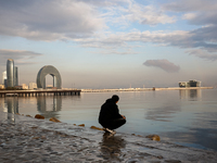 A man sits on Caspian Sea Boulevard in Baku in front of landmark architecture, Azerbaijan on November 9, 2024. (