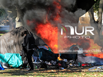 A person tries to recover belongings from a fire that engulfs tents at a homeless encampment in Gage Park, in Hamilton, Ontario, on November...