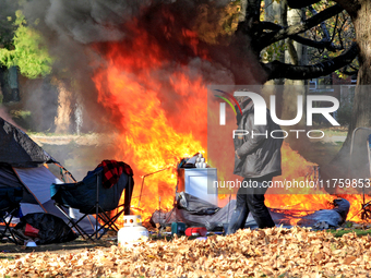 A person tries to recover belongings from a fire that engulfs tents at a homeless encampment in Gage Park, in Hamilton, Ontario, on November...