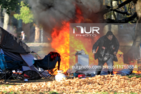 A person tries to recover belongings from a fire that engulfs tents at a homeless encampment in Gage Park, in Hamilton, Ontario, on November...