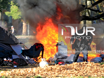 A person tries to recover belongings from a fire that engulfs tents at a homeless encampment in Gage Park, in Hamilton, Ontario, on November...