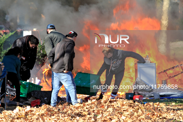 People try to recover belongings from a fire that engulfs tents at a homeless encampment in Gage Park, in Hamilton, Ontario, on November 9,...