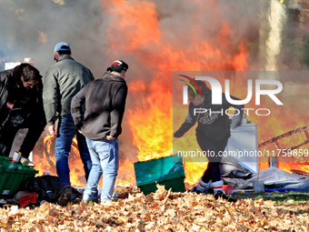 People try to recover belongings from a fire that engulfs tents at a homeless encampment in Gage Park, in Hamilton, Ontario, on November 9,...