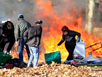 People try to recover belongings from a fire that engulfs tents at a homeless encampment in Gage Park, in Hamilton, Ontario, on November 9,...