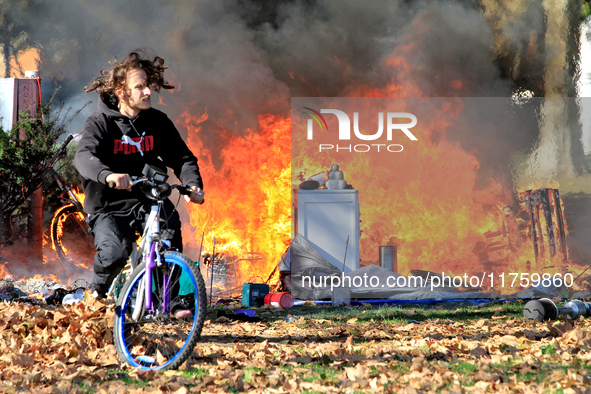 A person recovers a bicycle and cycles away from a fire that engulfs tents at a homeless encampment in Gage Park, in Hamilton, Ontario, on N...