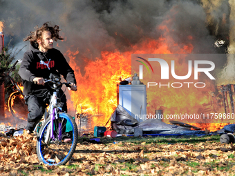 A person recovers a bicycle and cycles away from a fire that engulfs tents at a homeless encampment in Gage Park, in Hamilton, Ontario, on N...