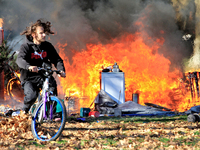 A person recovers a bicycle and cycles away from a fire that engulfs tents at a homeless encampment in Gage Park, in Hamilton, Ontario, on N...